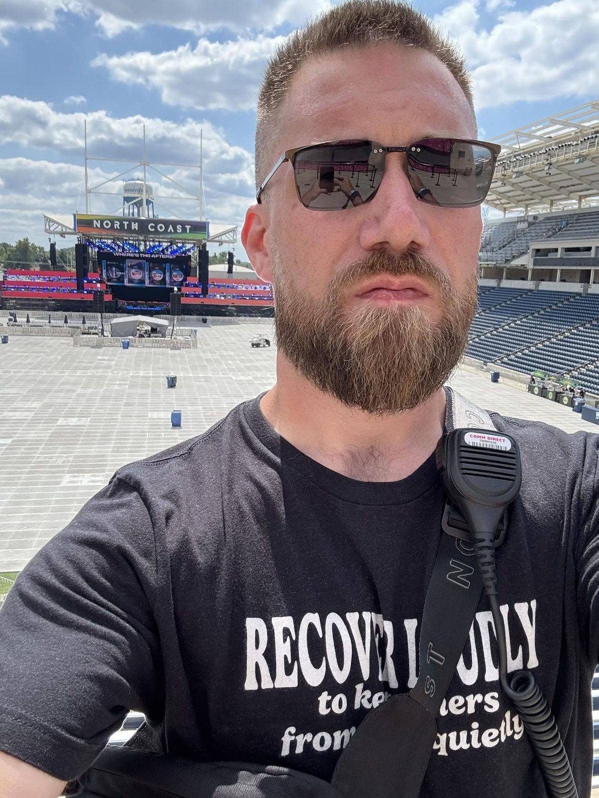 Sam at North Coast Music Festival with a radio mic clipped to his shirt, the main stage and empty stadium floor behind him